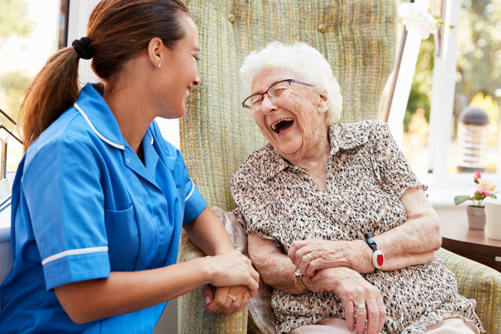 Compassionate caregiver at Adult Family Center of Moses Lake providing personalized eldercare Seattle families trust, featuring a staff member in blue scrubs assisting an elderly woman.